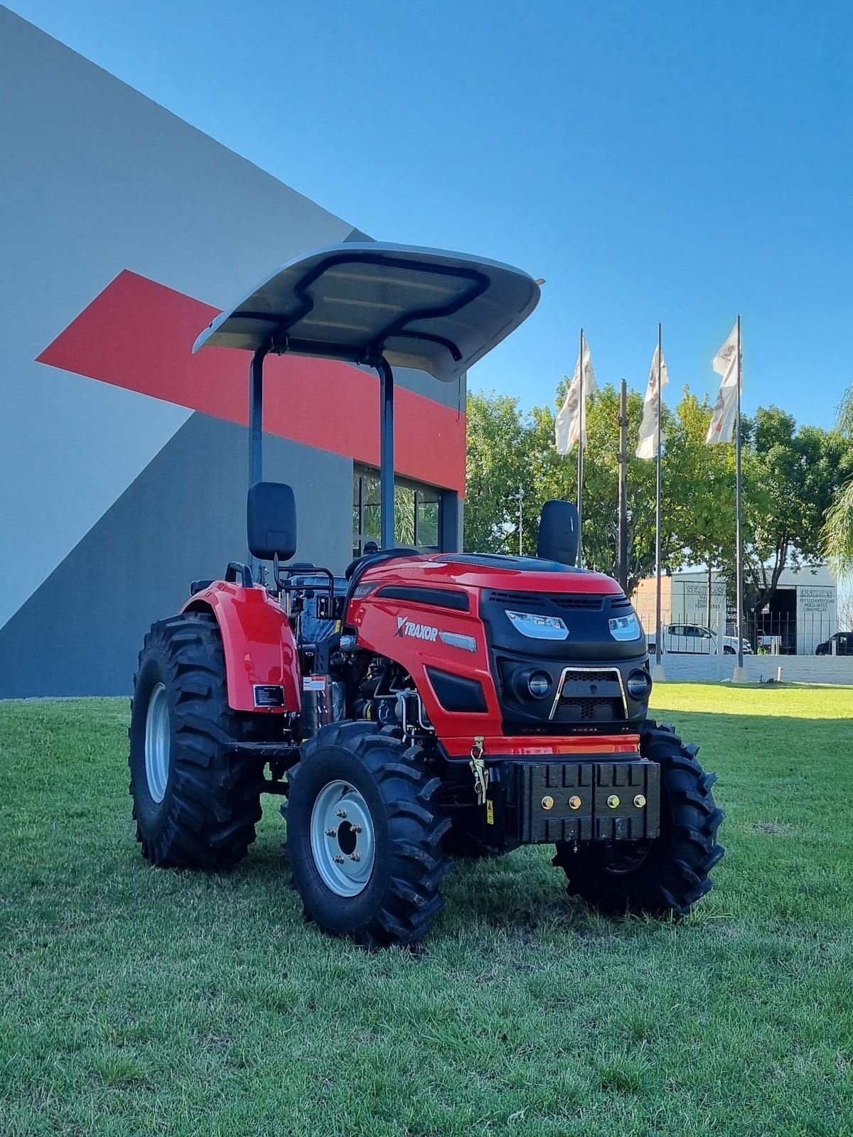 Tractor compacto Traxor TRX 50 P de frente y de costado, junto a un galpón